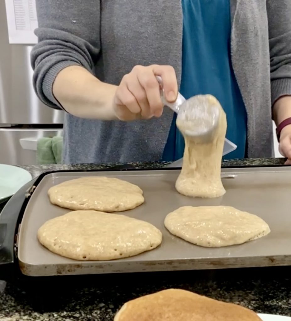 woman pouring overnight sourdough pancake batter onto griddle with measuring cup